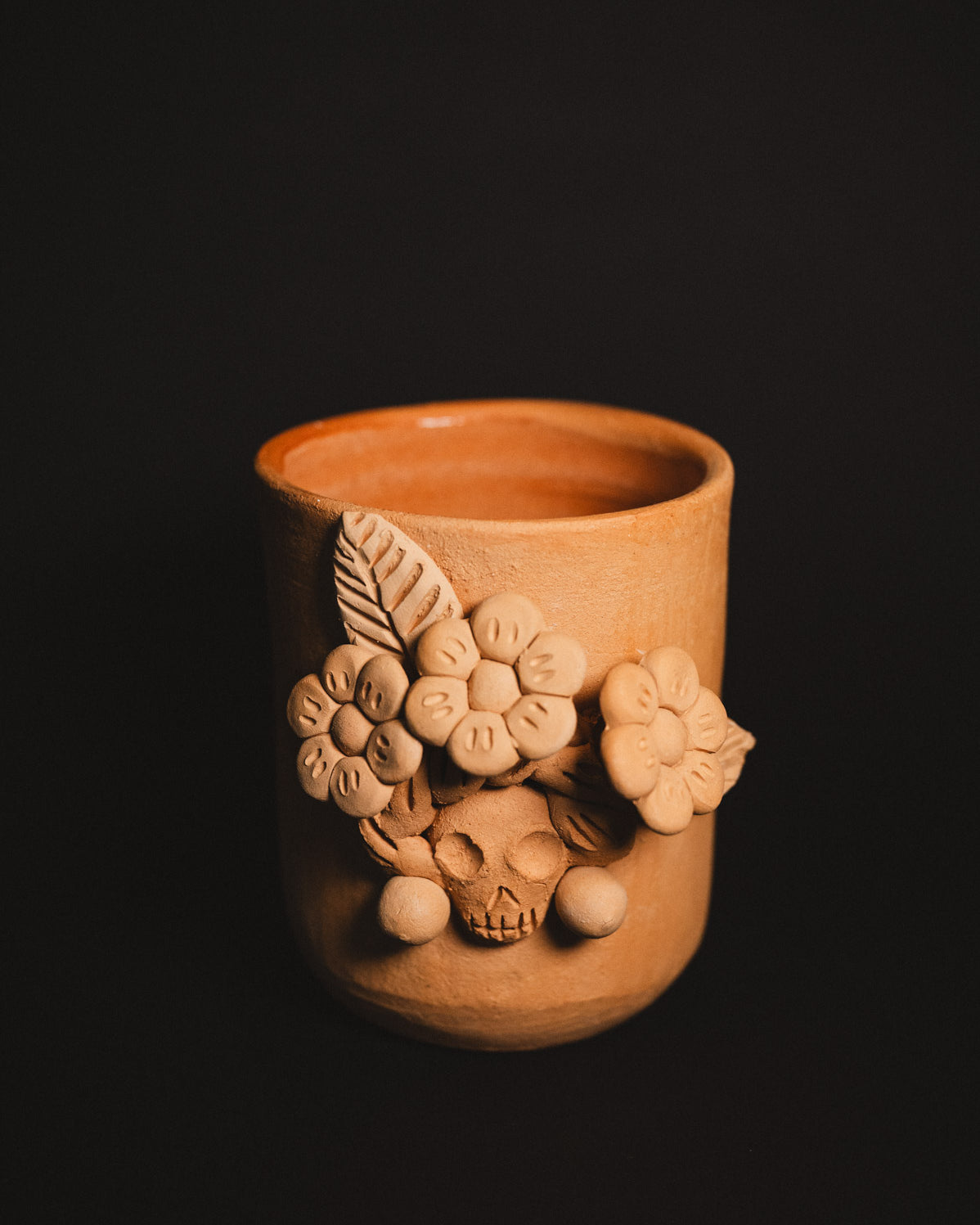 Terracotta cup with floral and skull designs on a black background
