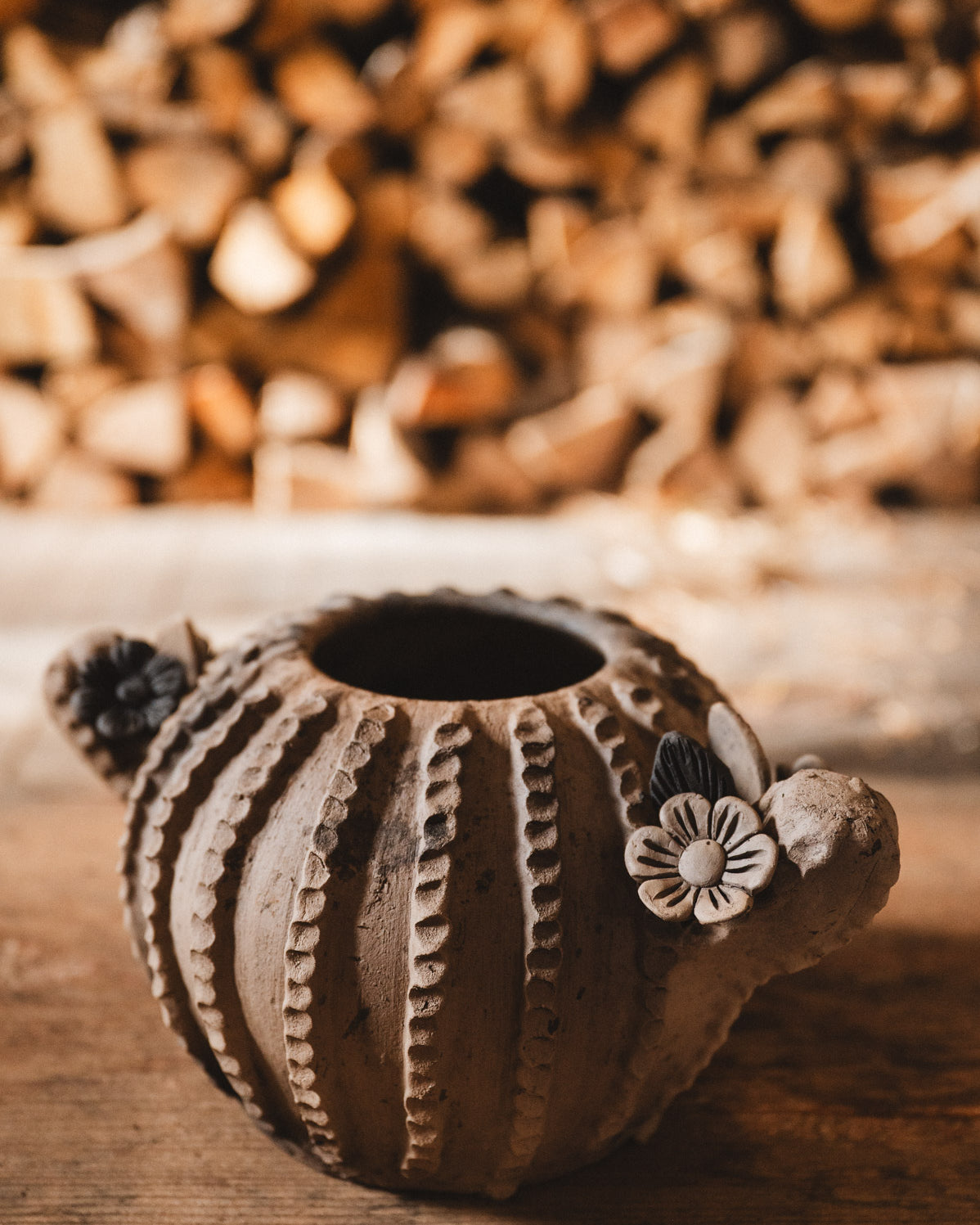 Ceramic cactus planter with floral design on a wooden surface with blurred woodpile background
