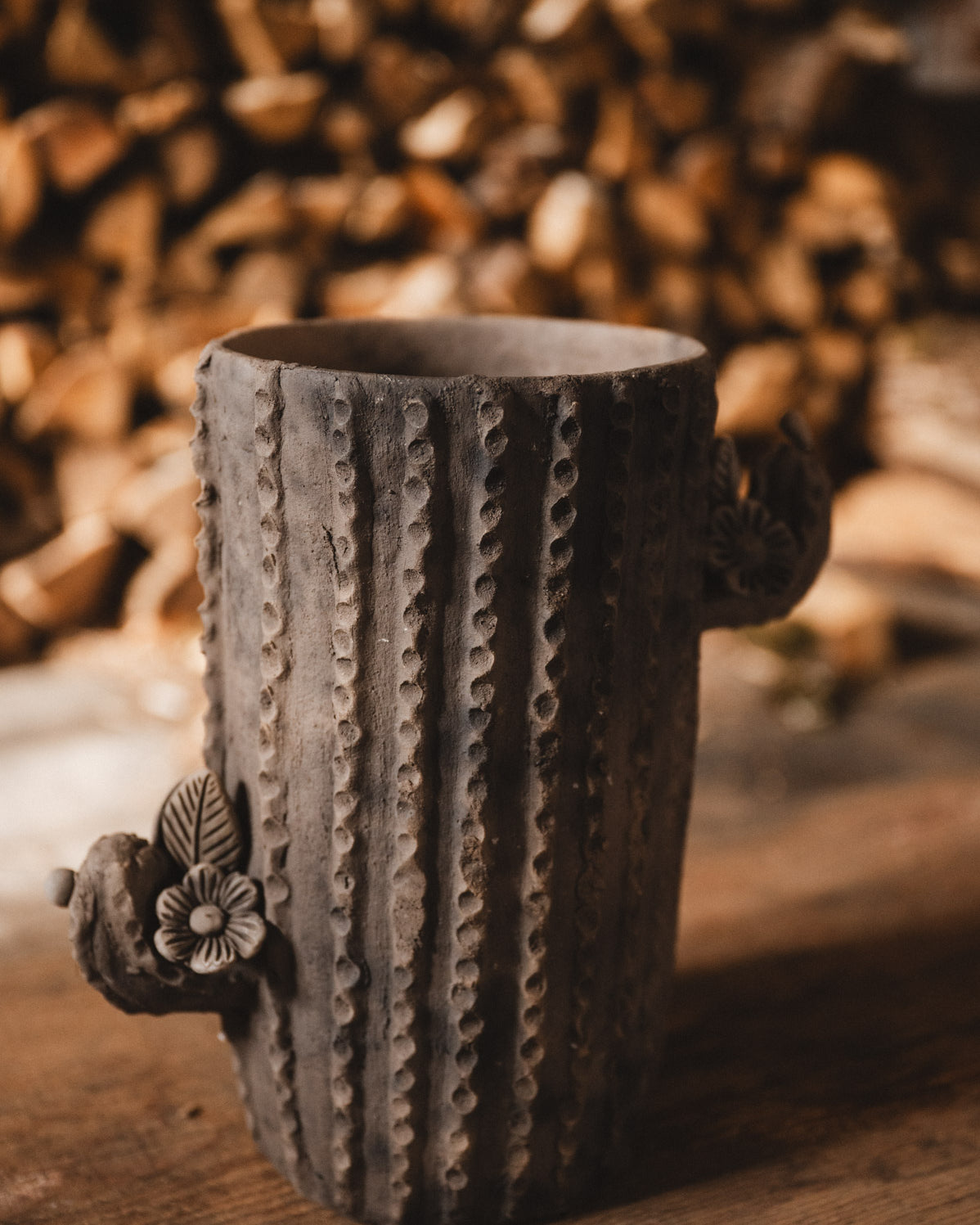 Ceramic cactus-shaped planter with textured design on a wooden surface with stacked firewood in the background.