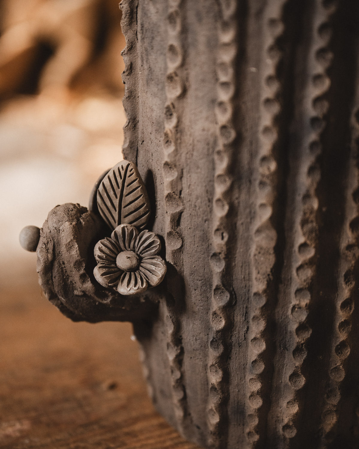 Ceramic cactus-shaped planter with textured design on a wooden surface with stacked firewood in the background.