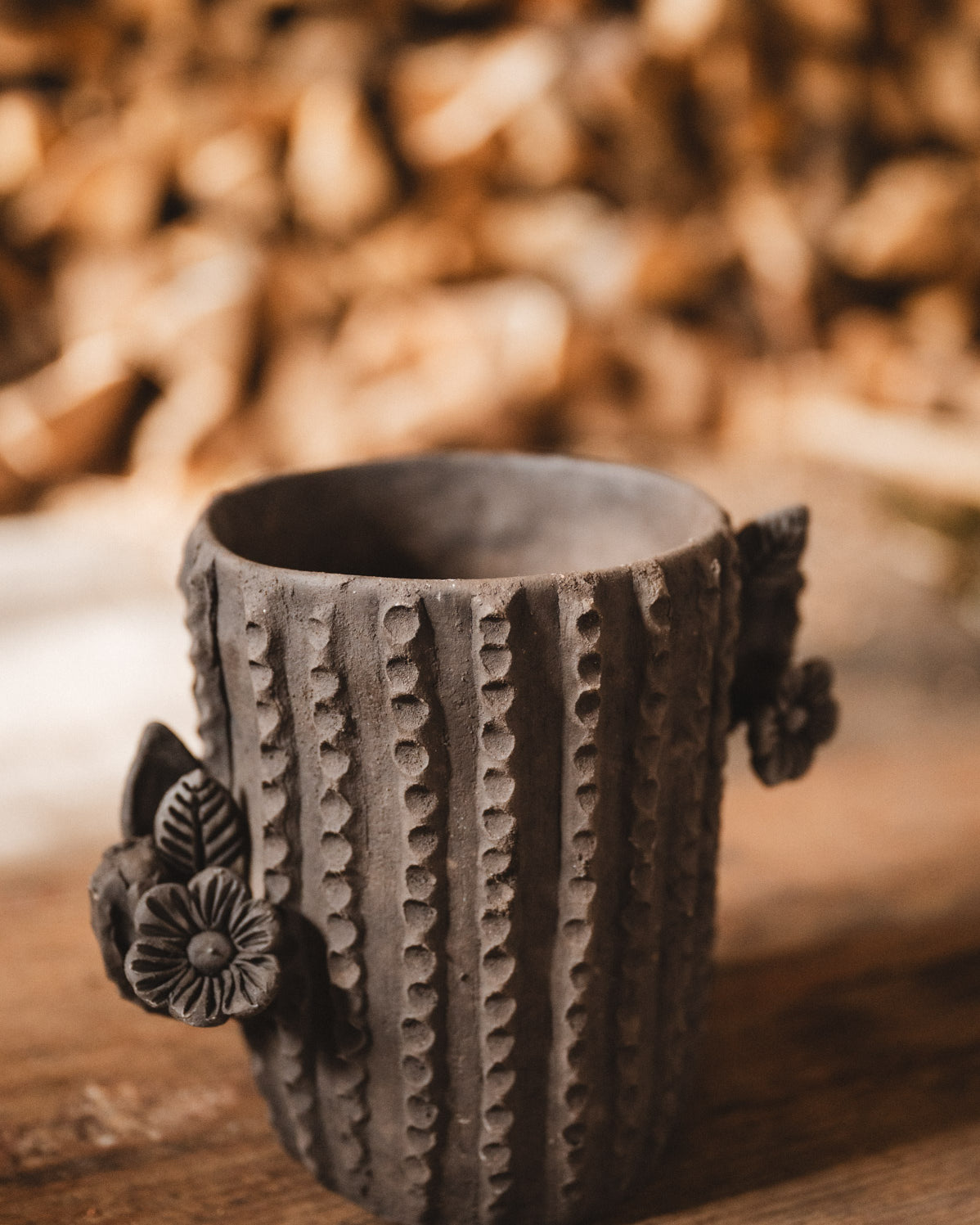Ceramic cactus-shaped planter with textured design on a wooden surface with stacked firewood in the background.