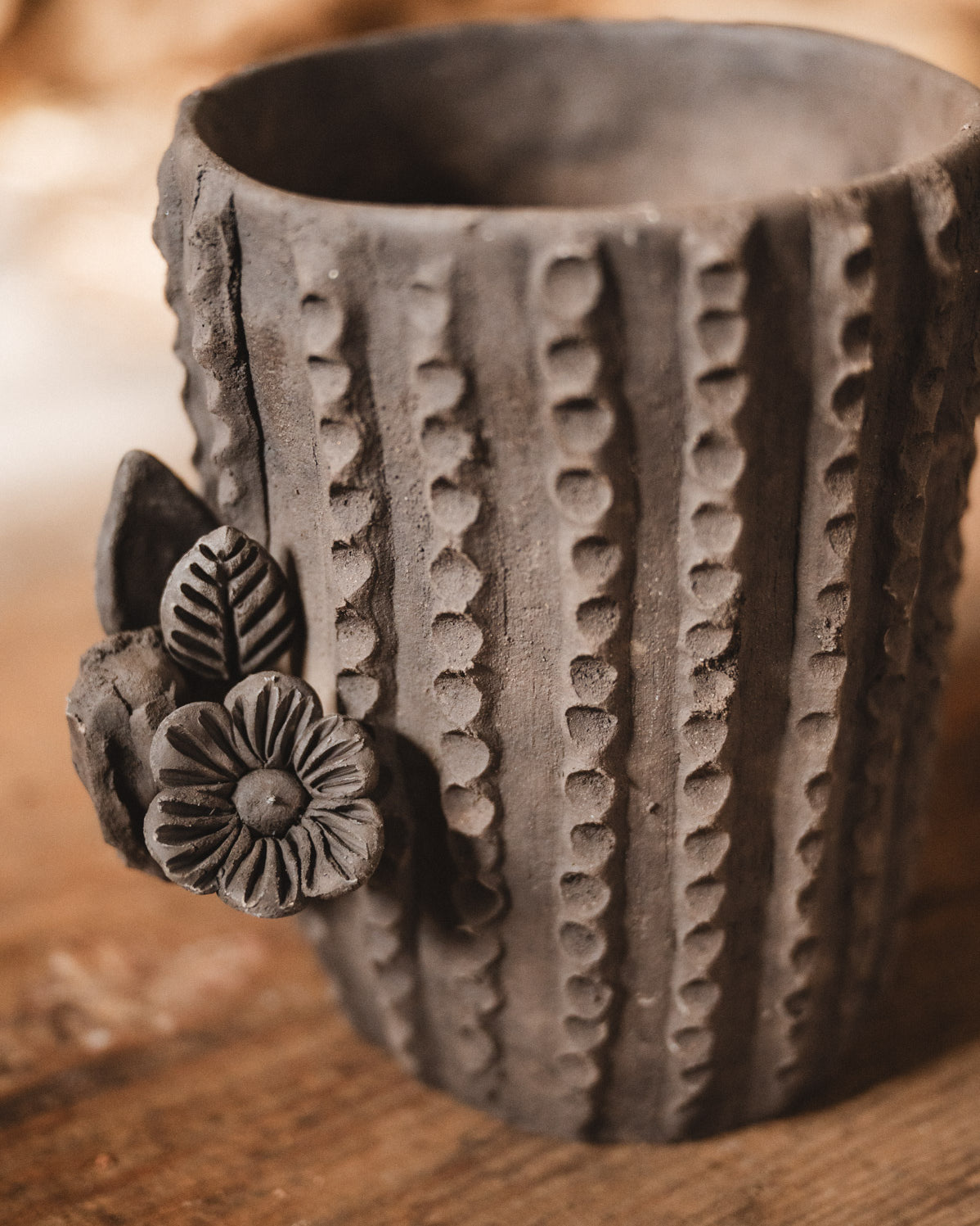 Ceramic cactus-shaped planter with textured design on a wooden surface with stacked firewood in the background.