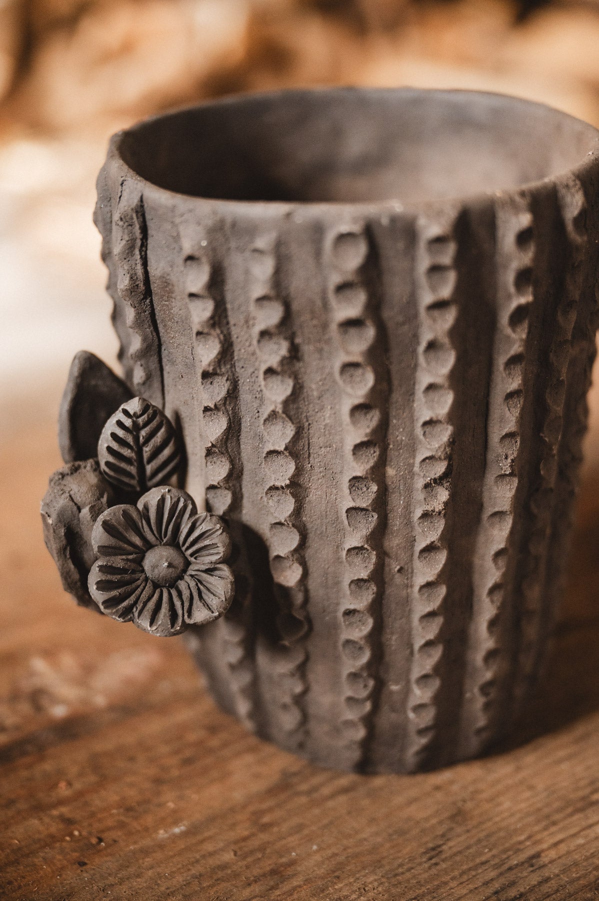Ceramic cactus-shaped planter with textured design on a wooden surface with stacked firewood in the background.