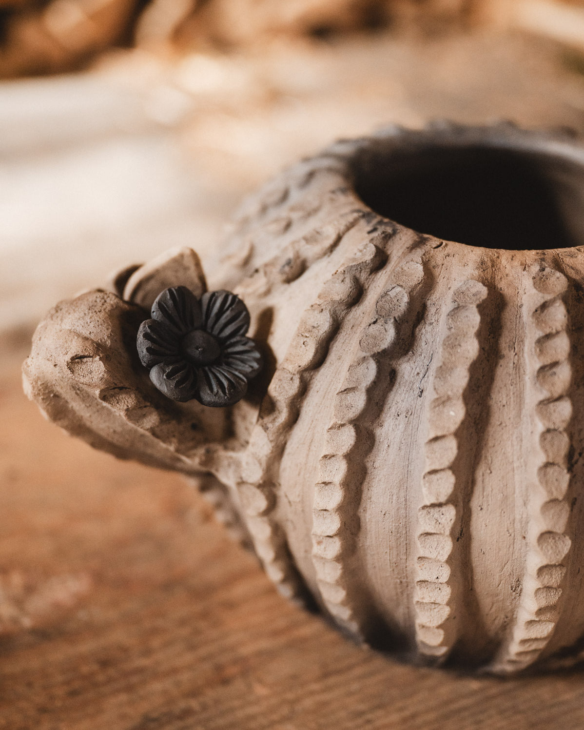 Ceramic cactus planter with floral design on a wooden surface with blurred woodpile background