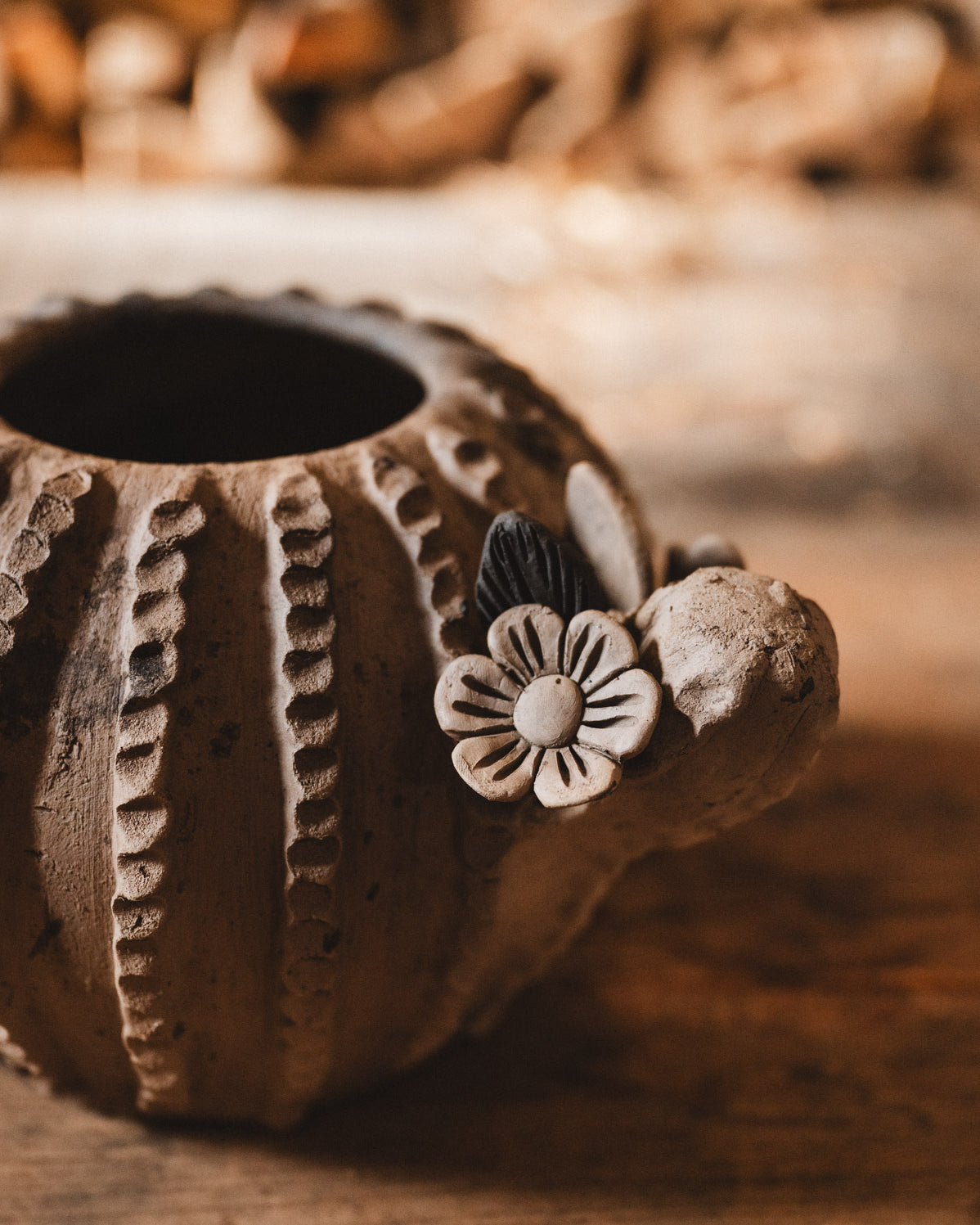 Ceramic cactus planter with floral design on a wooden surface with blurred woodpile background