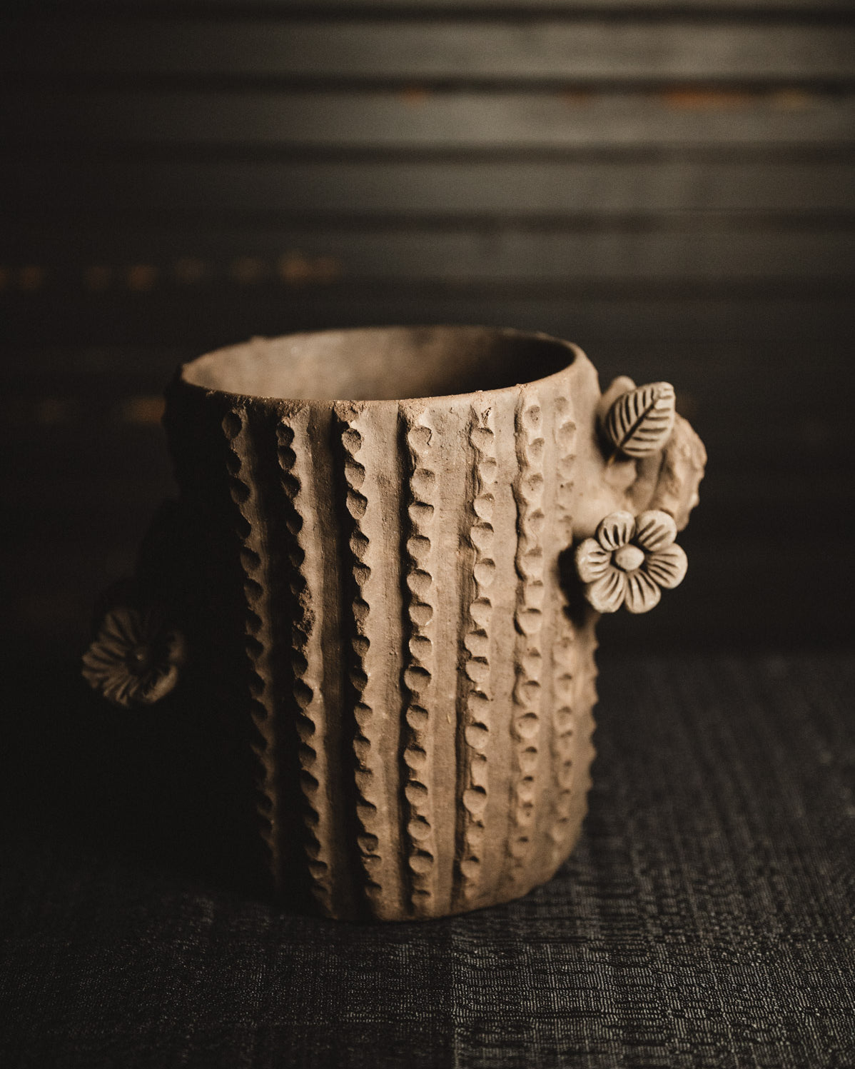 Ceramic planter with textured design and floral handle on a dark background