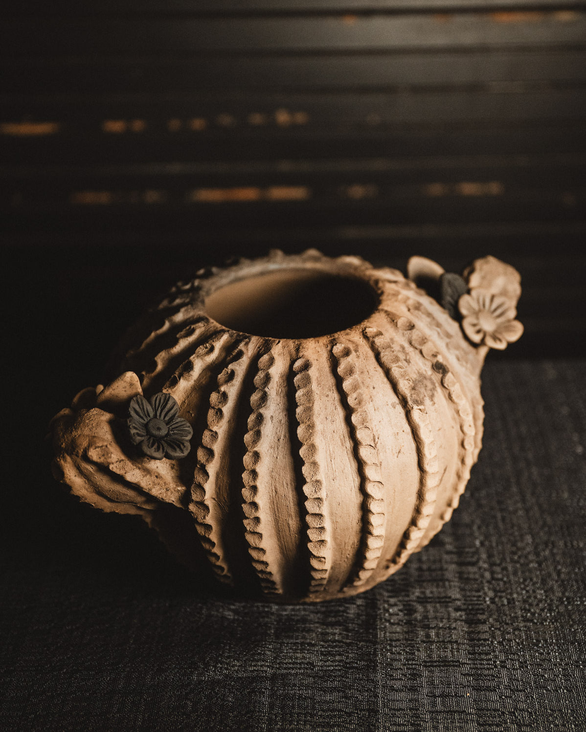 Ceramic planter with textured surface and floral decorations on a dark background