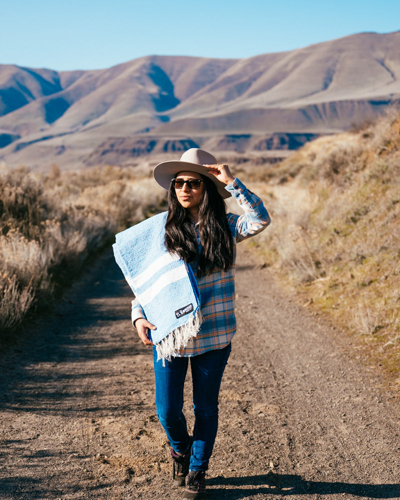 Girl walking down path in the high desert with blue blanket on her shoulder