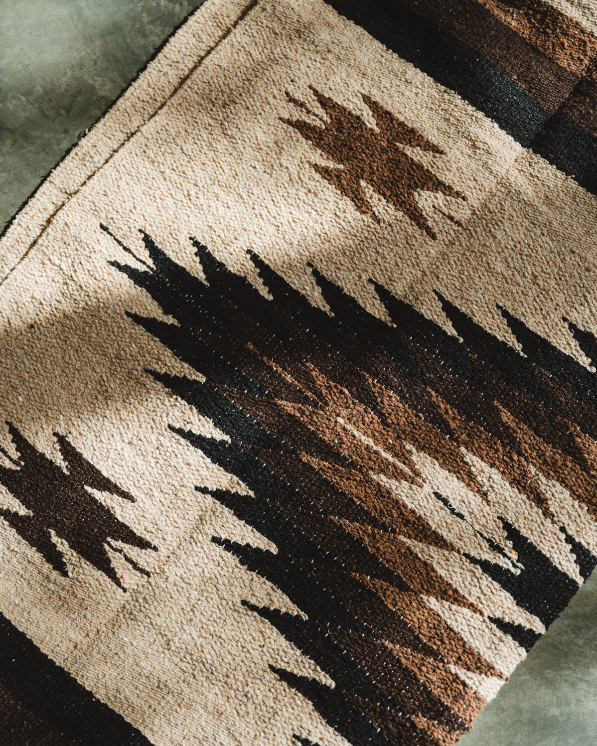 Handwoven brown and beige diamond mexican blanket folded on ground