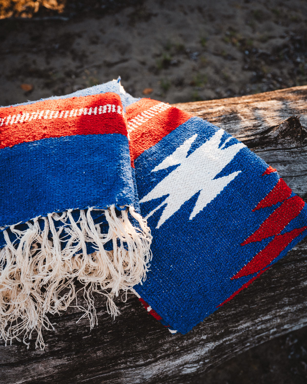 Red, blue, and white Mexican blanket on a wooden log outdoors
