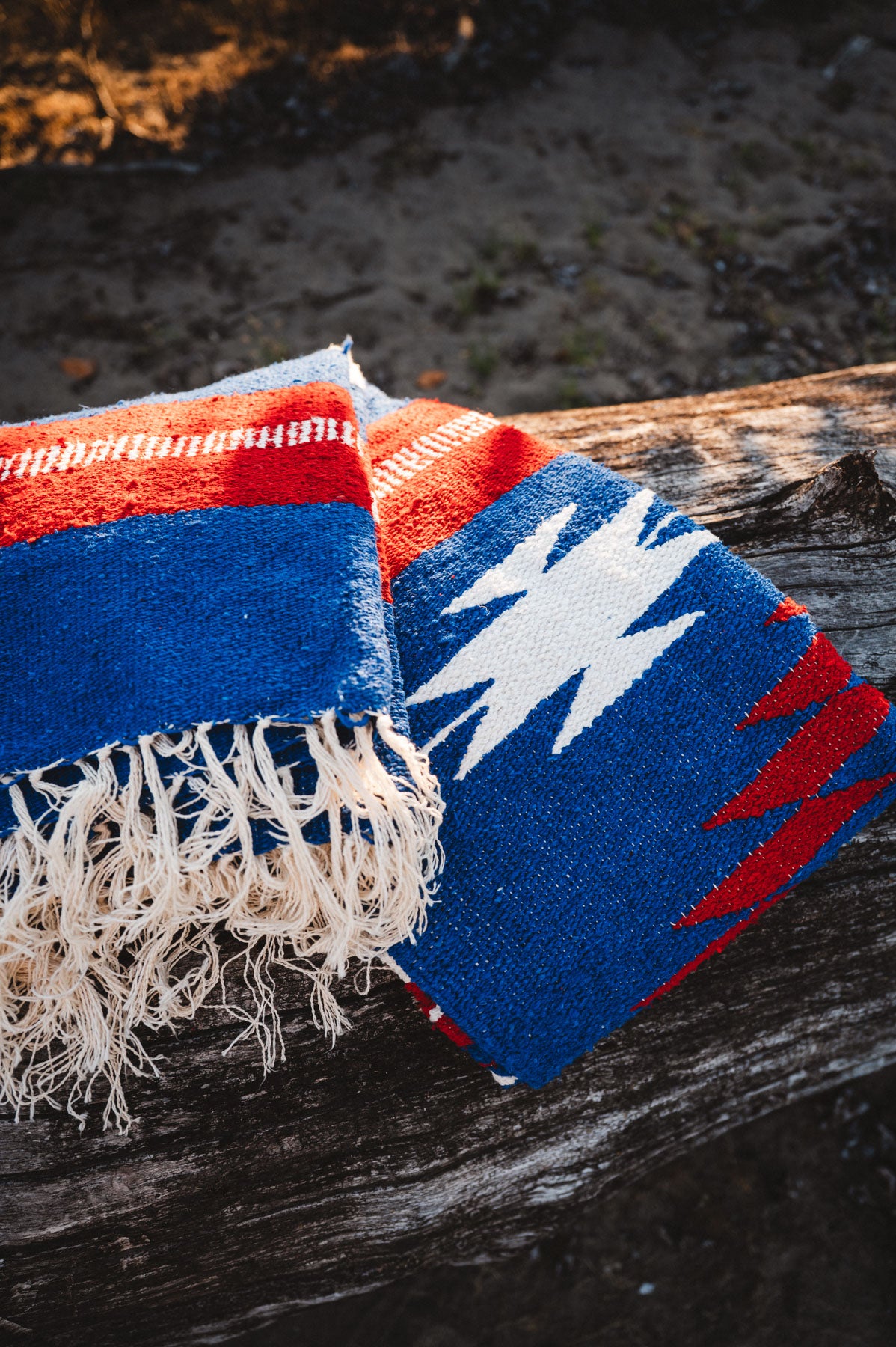 Red, blue, and white Mexican blanket on a wooden log outdoors