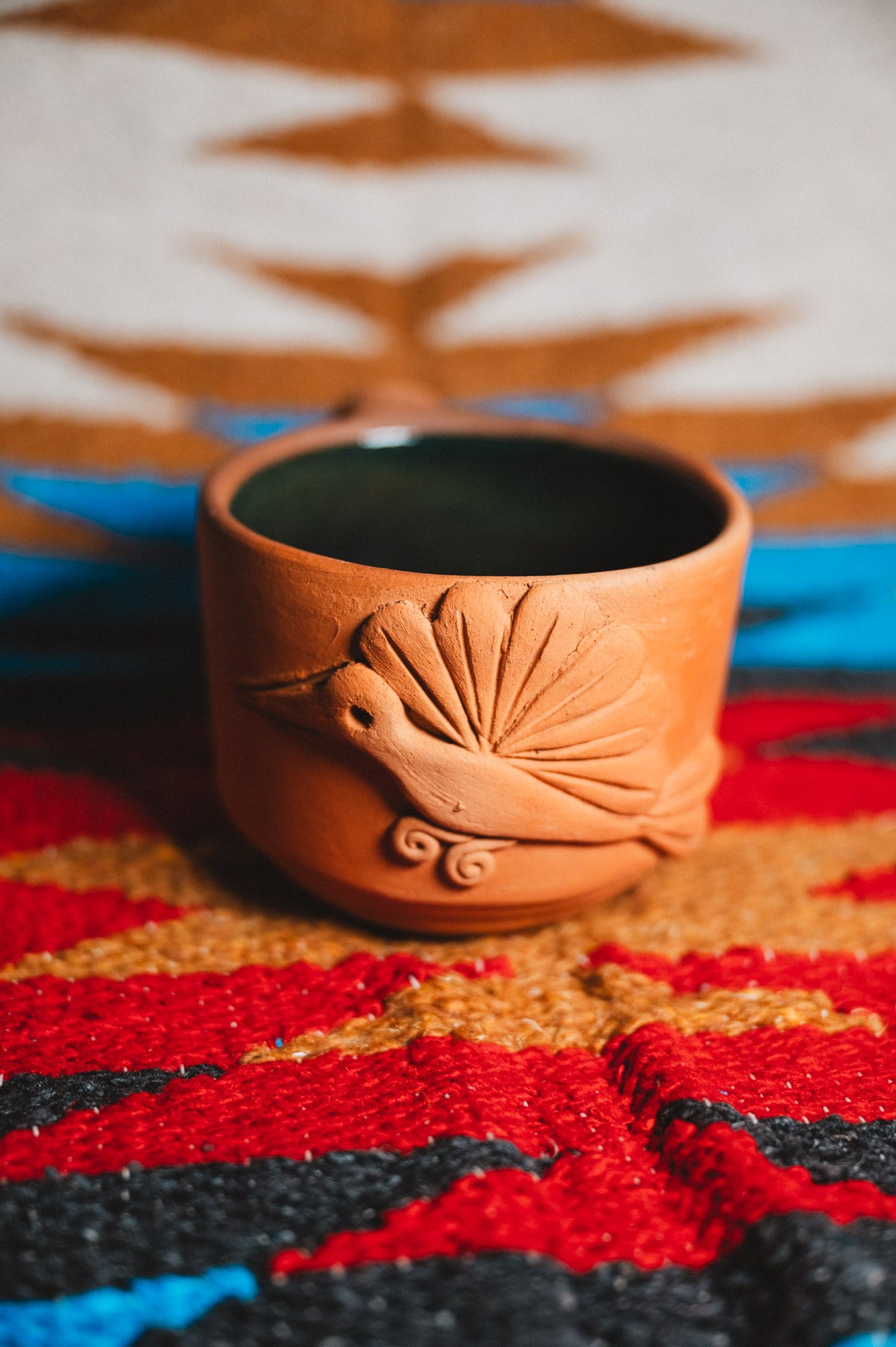 Terracotta cup with decorative design on a colorful patterned fabric background
