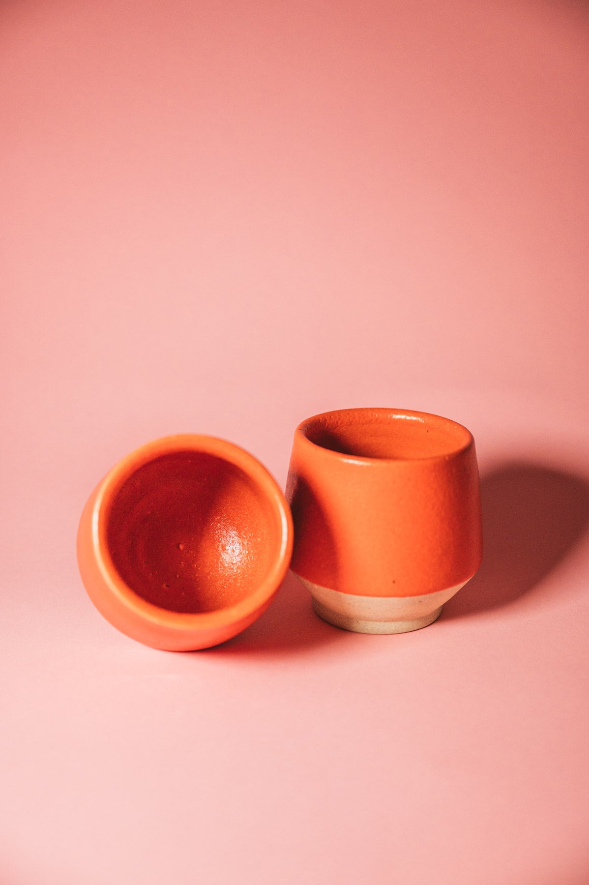 Two orange ceramic cups on a pink background