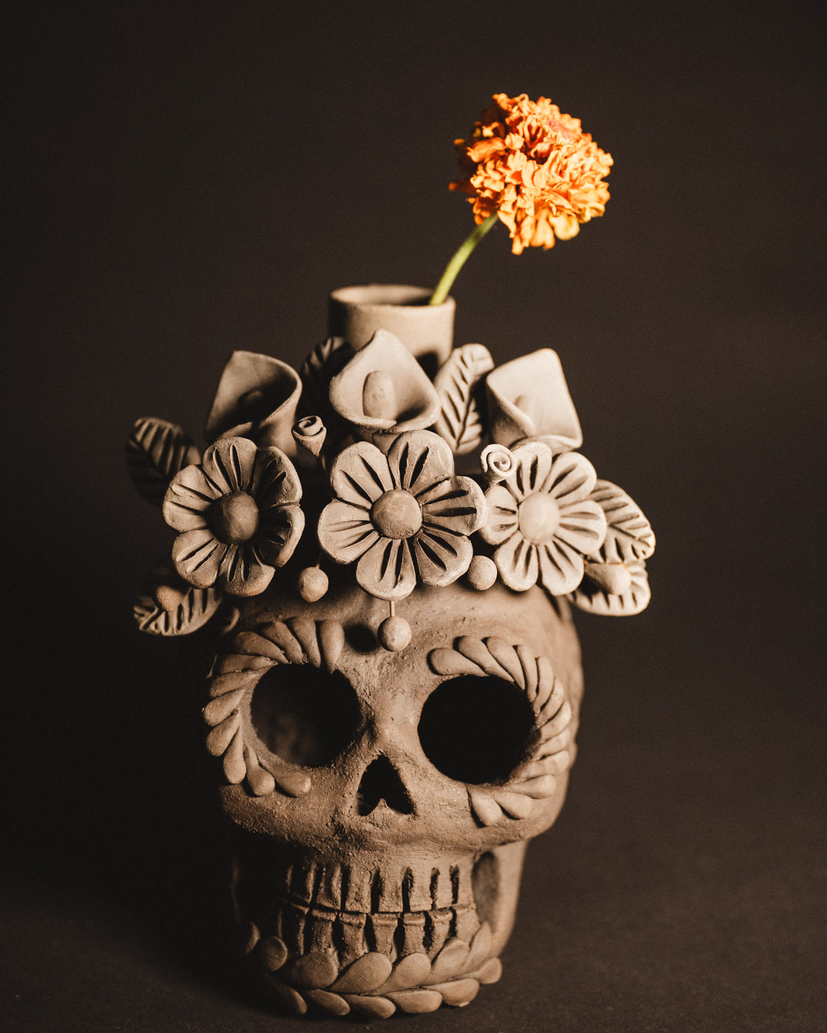 Ceramic skull vase with floral designs and a single orange flower on a dark background