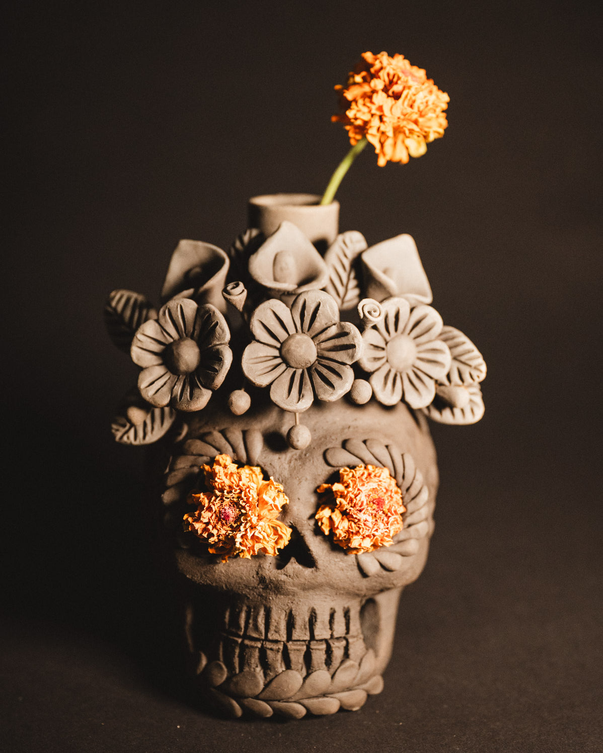 Ceramic skull vase with floral designs and orange flowers against a dark background
