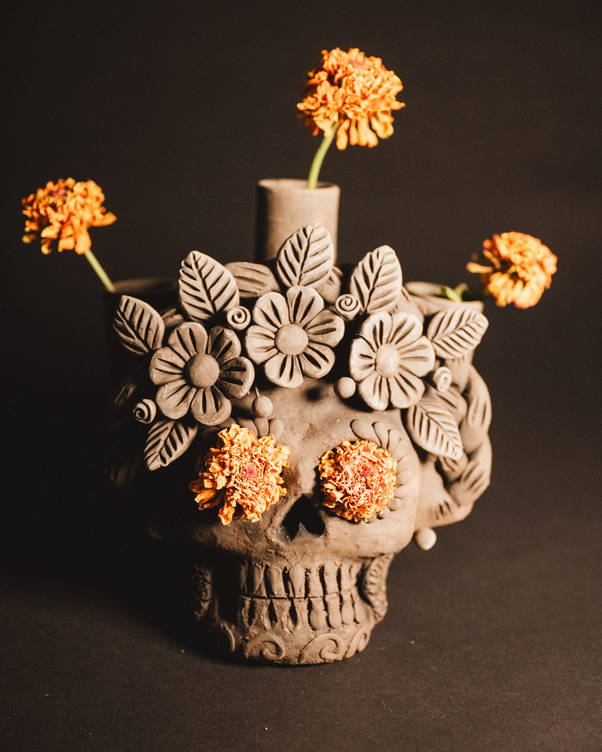 Ceramic skull vase with floral designs and orange flowers on a dark background