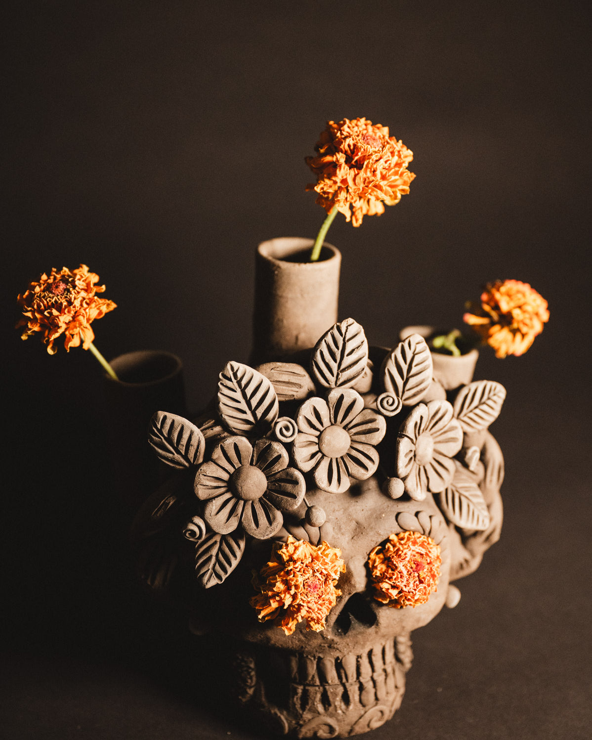 Ceramic skull vase with floral designs and orange flowers on a dark background