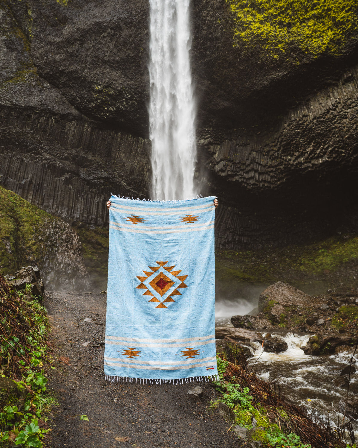 Blue patterned rug draped over a natural rock formation with water flowing through.