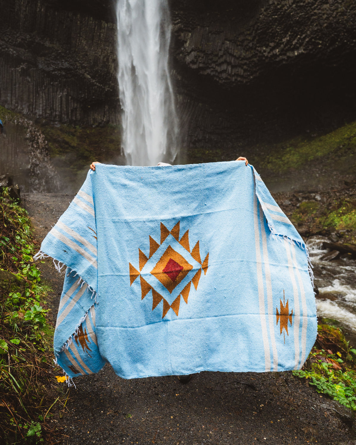 Blue blanket with a geometric pattern draped over a chair in front of a waterfall.