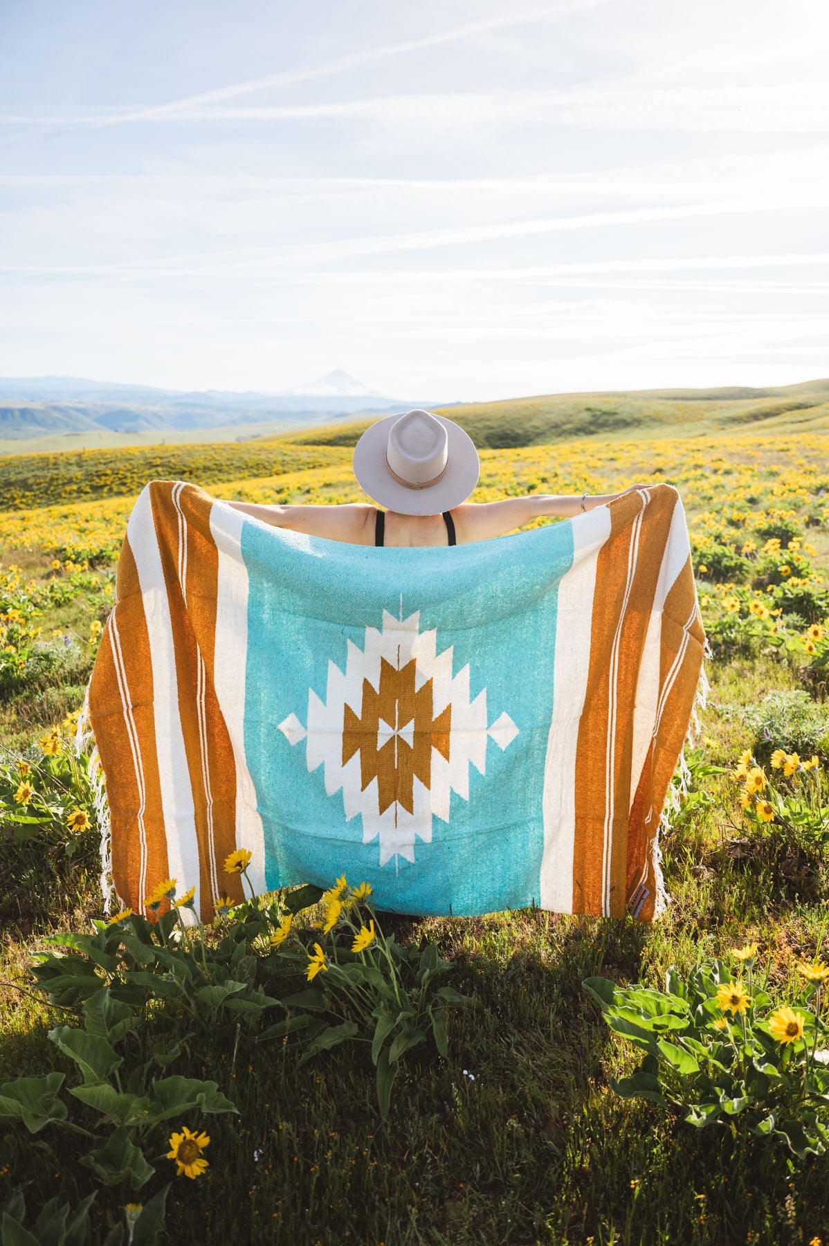 Person sitting on a blanket with a colorful pattern in a field of wildflowers