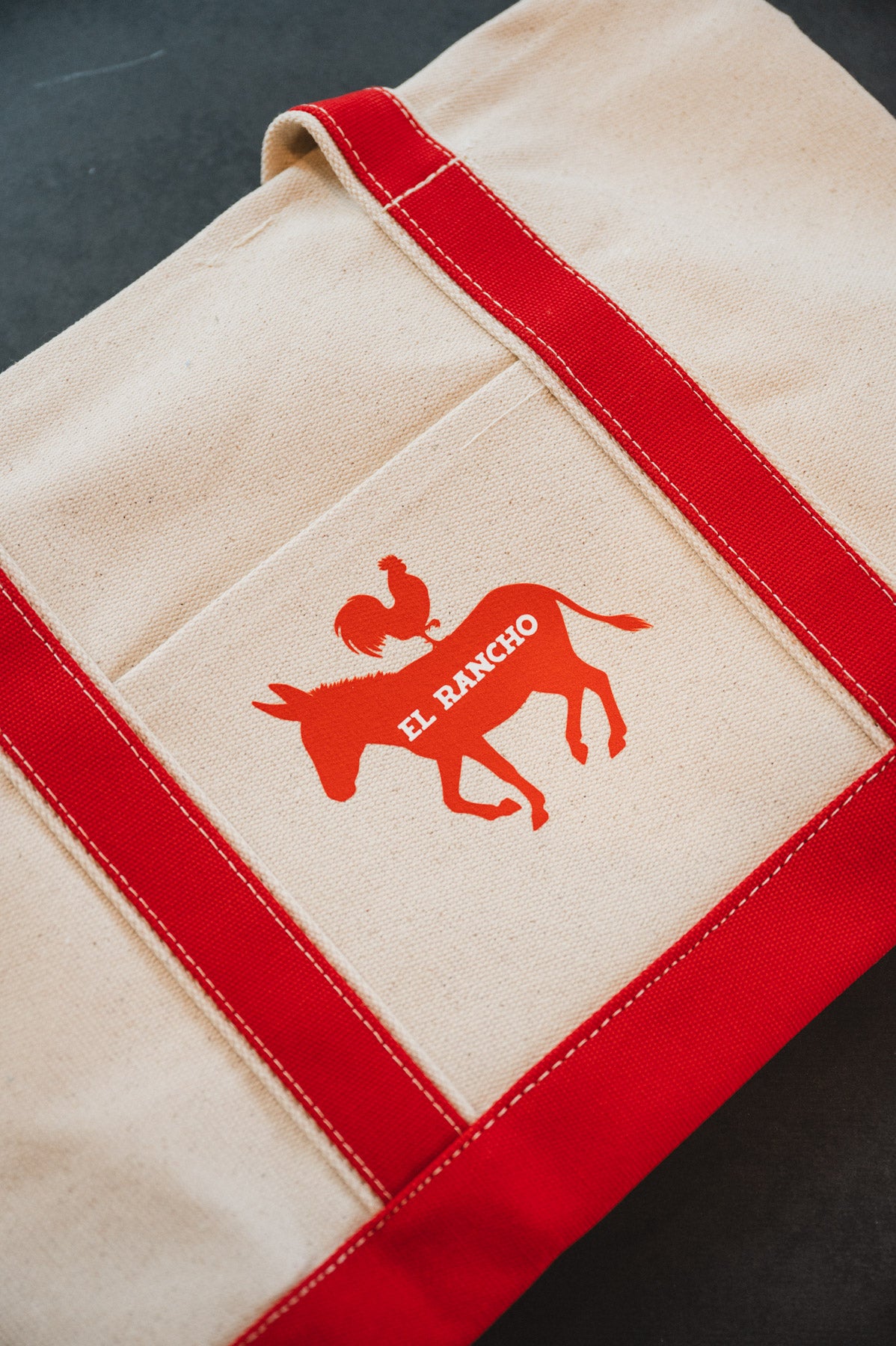 Beige bag with red accents and a logo on a dark surface