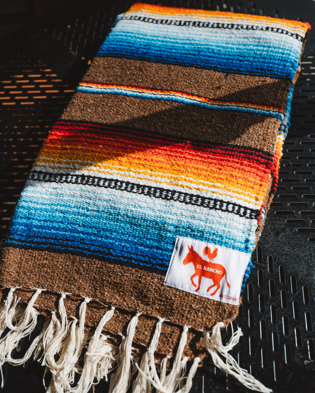 Colorful woven blanket with fringes on a dark surface