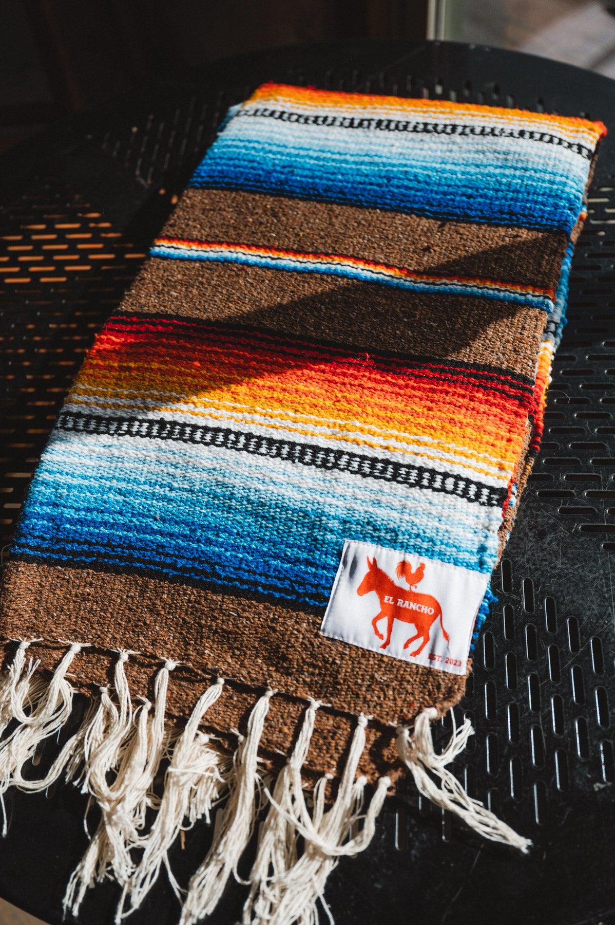 Colorful woven blanket with fringes on a dark surface