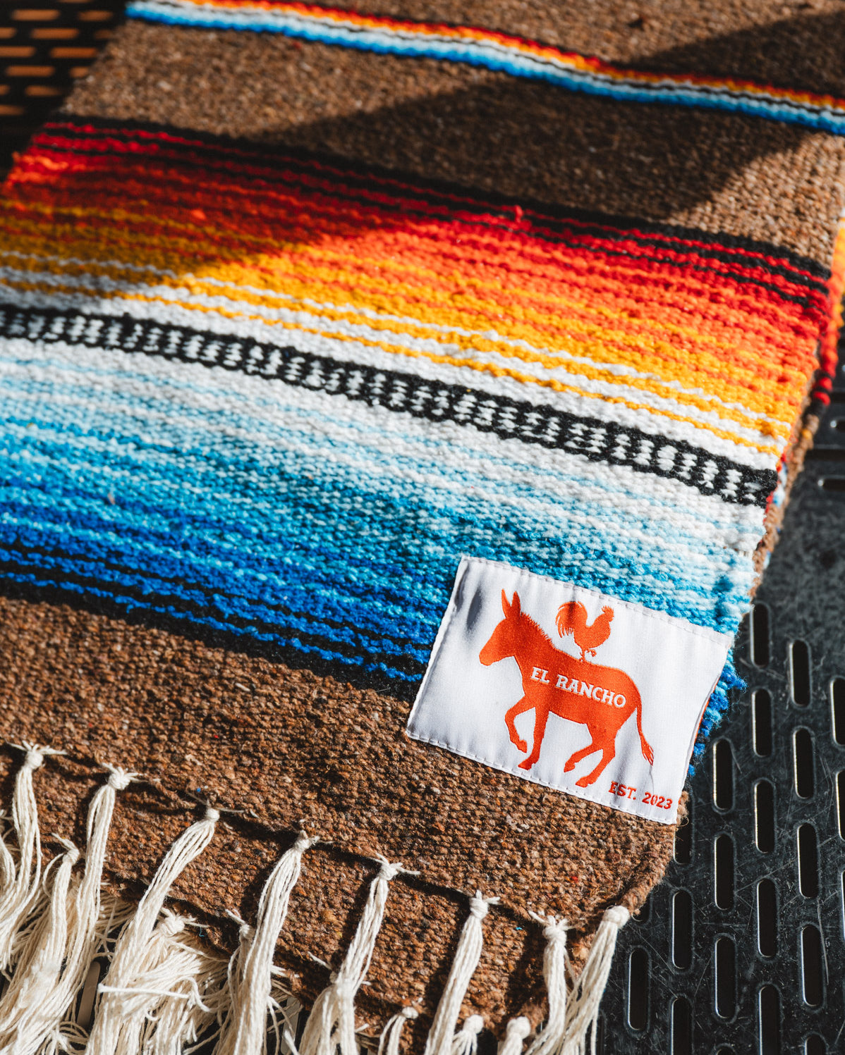 Colorful woven blanket with a brand label on a textured surface