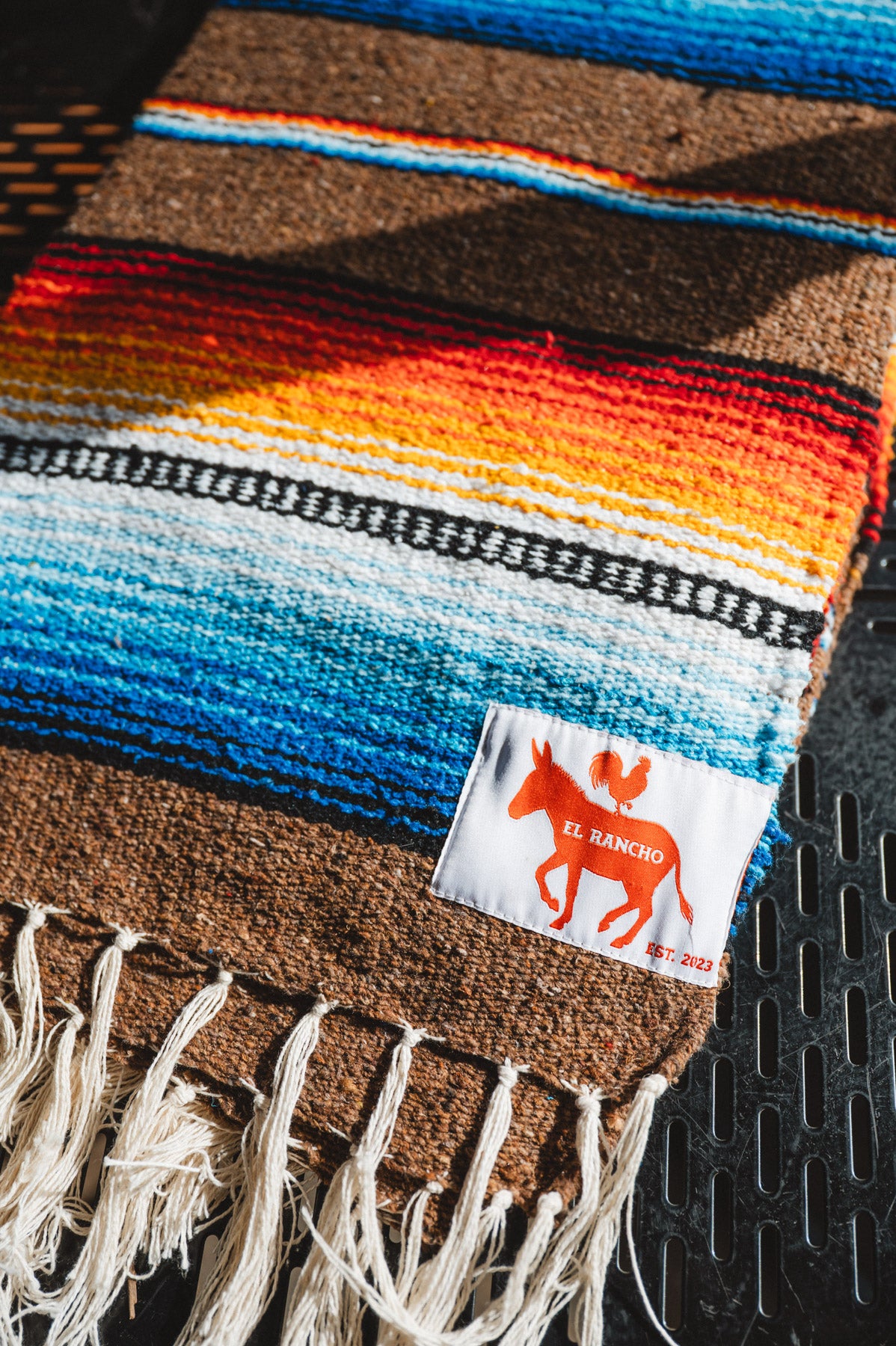 Colorful woven blanket with a brand label on a textured surface