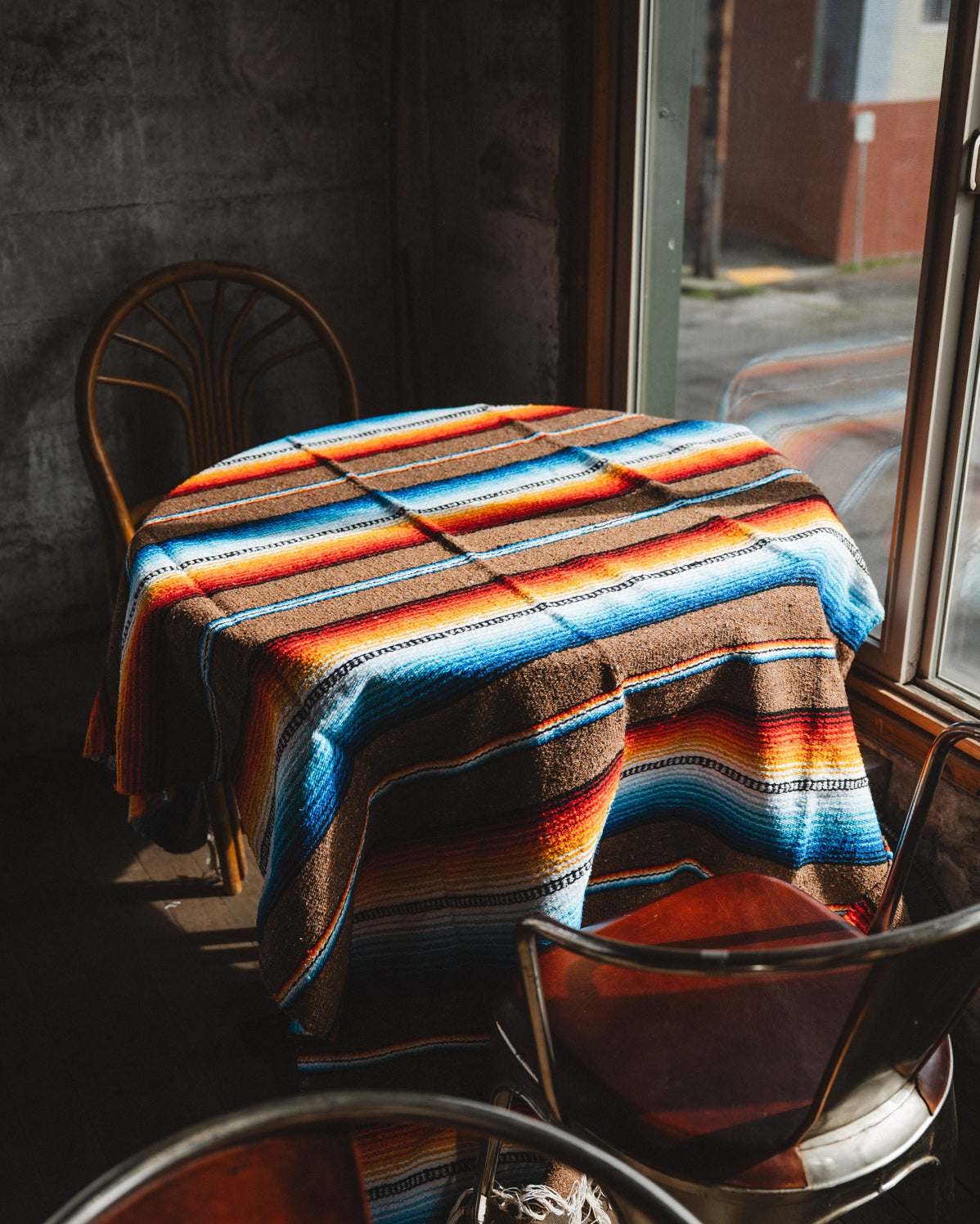 Colorful striped blanket draped over a table with chairs in a dimly lit room.