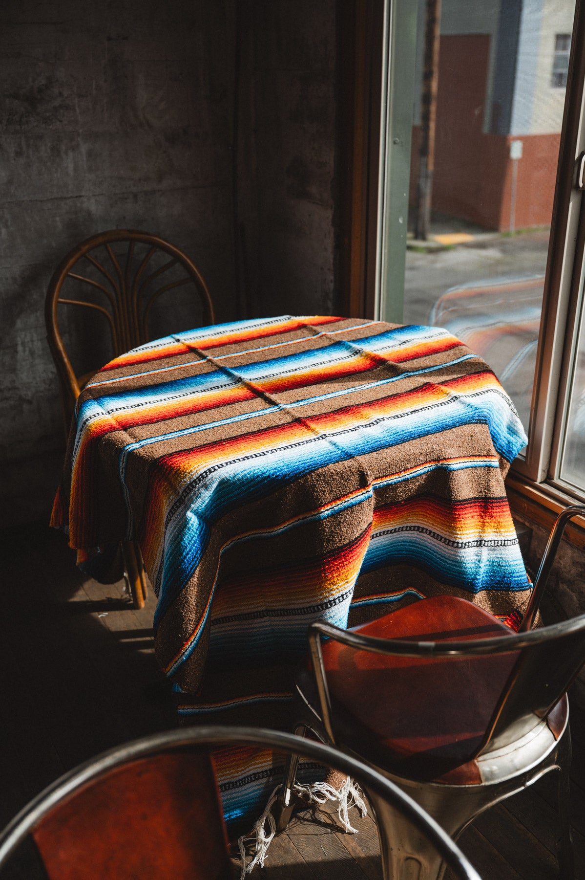 Colorful striped blanket draped over a table with chairs in a dimly lit room.