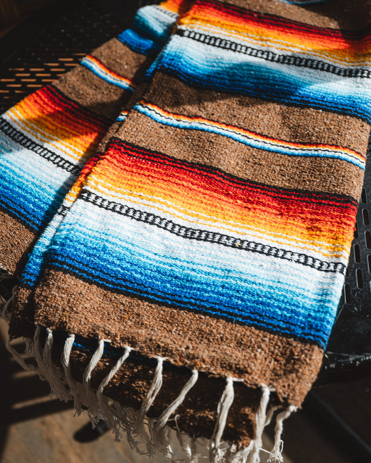 Colorful striped blanket with fringes on a dark surface