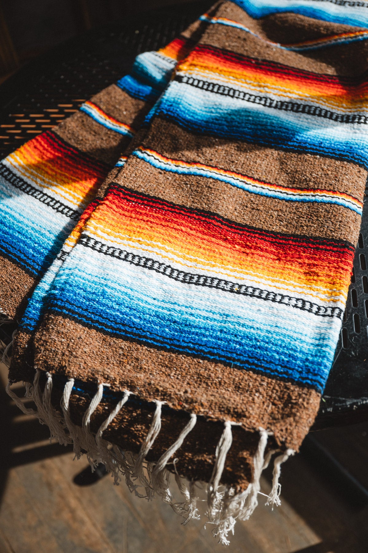 Colorful striped blanket with fringes on a dark surface