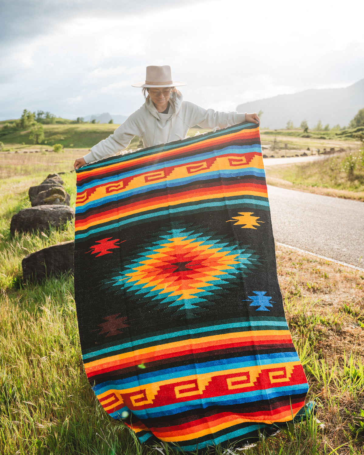 Mexican woman holding multicolored handwoven mexican blanket with greca designs