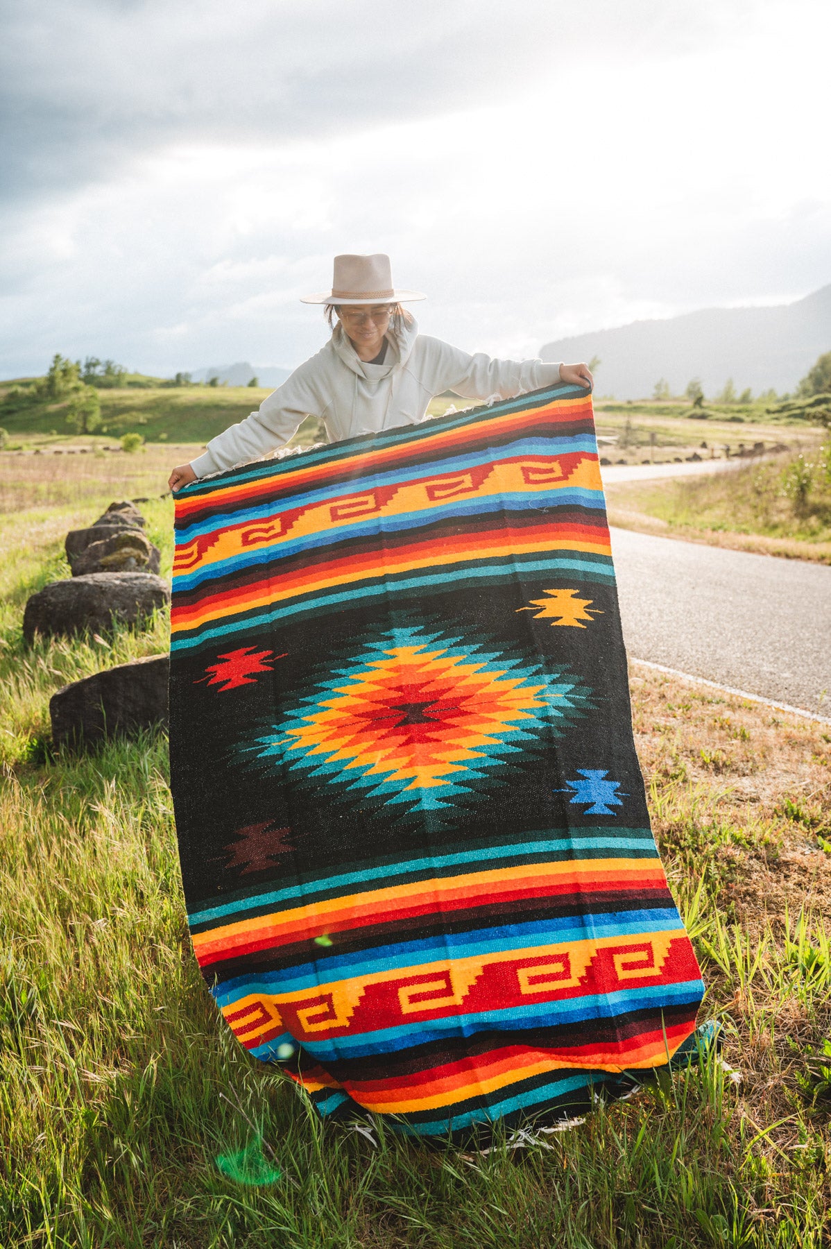 Mexican woman holding multicolored handwoven mexican blanket with greca designs