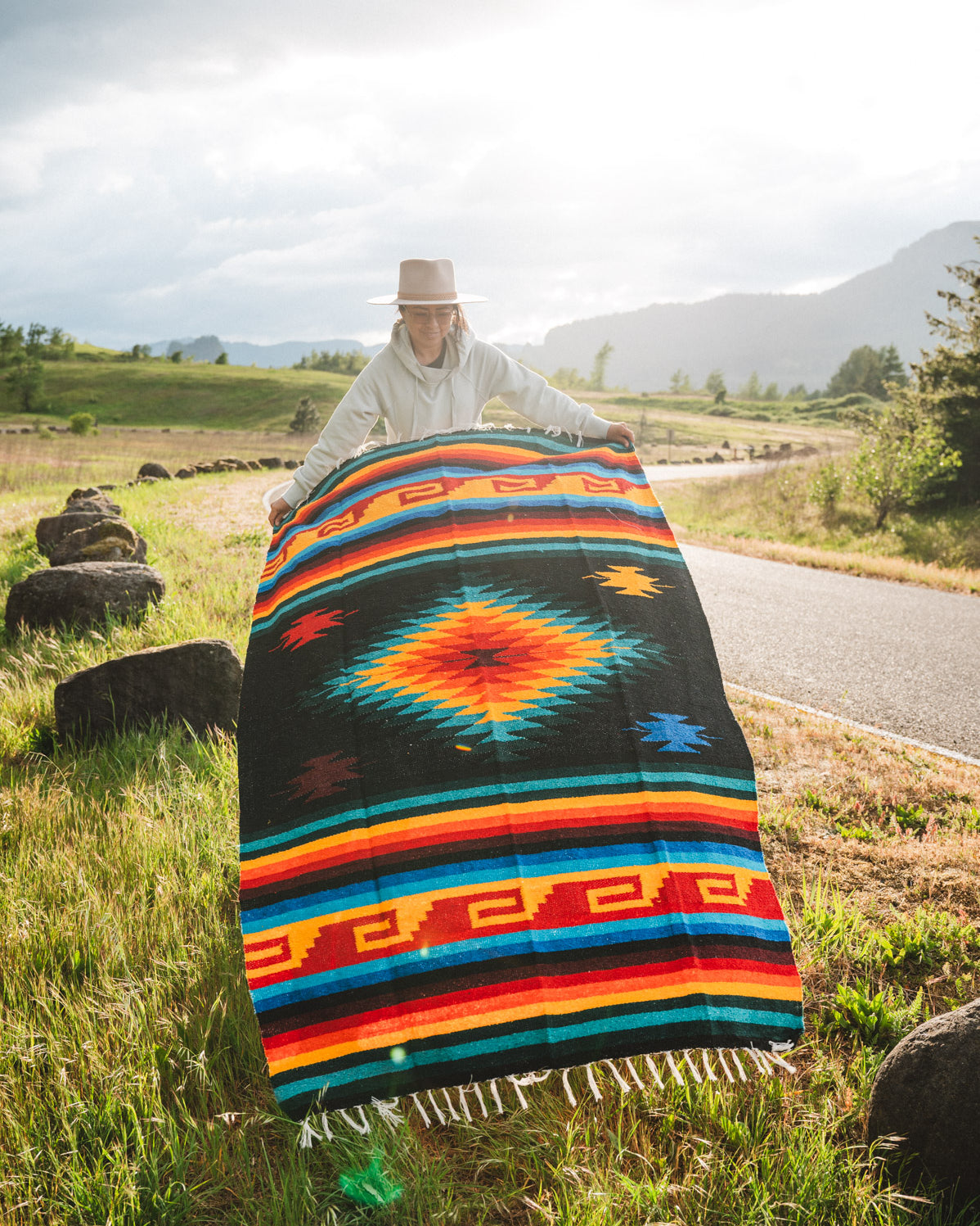 Mexican woman holding multicolored handwoven mexican blanket with greca designs