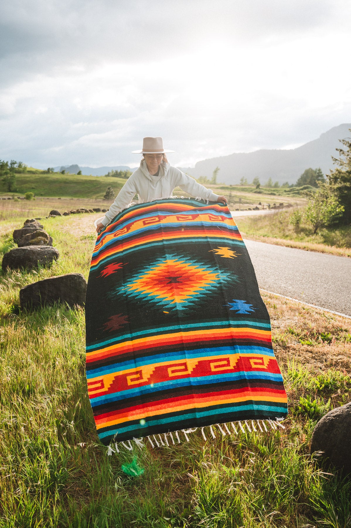 Mexican woman holding multicolored handwoven mexican blanket with greca designs