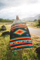Mexican woman holding multicolored handwoven mexican blanket with greca designs