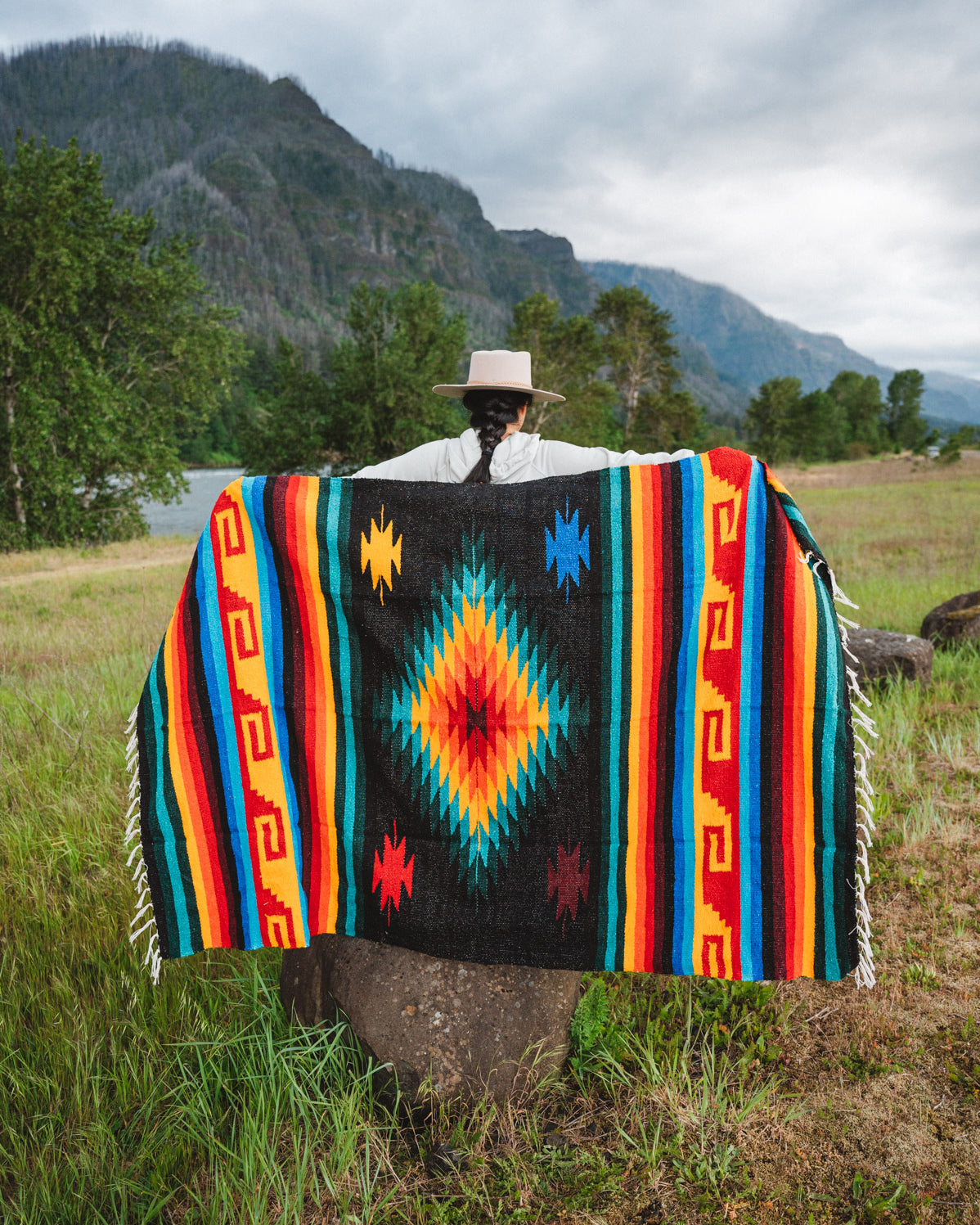 Mexican woman holding multicolored handwoven mexican blanket with greca designs