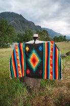Mexican woman holding multicolored handwoven mexican blanket with greca designs