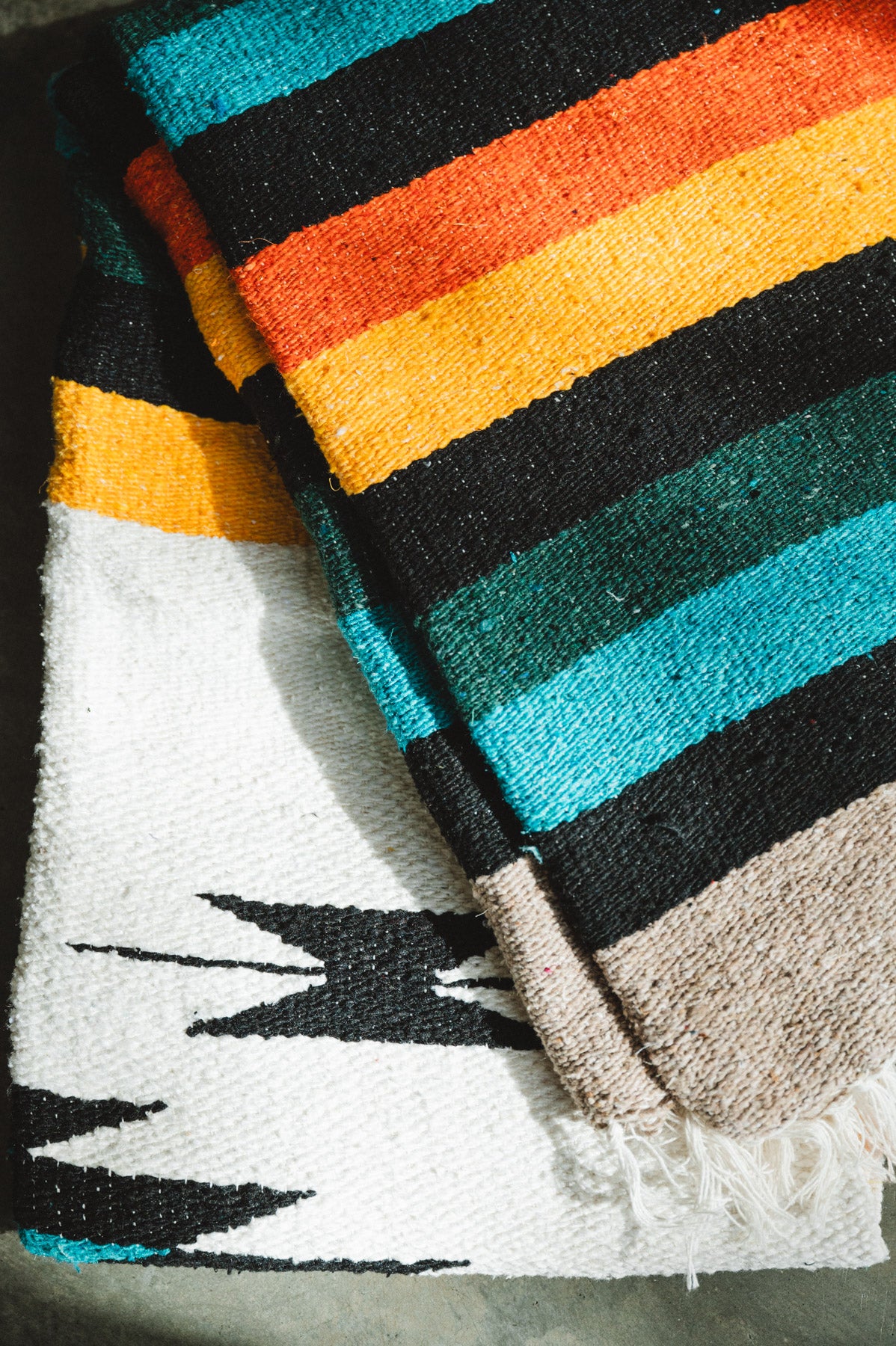 Green and white handwoven diamond mexican blanket folded on the ground