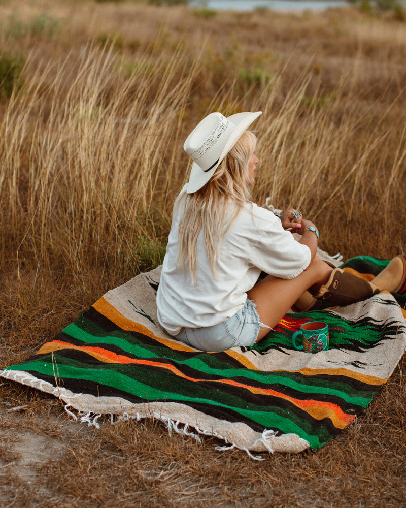 girl sitting on diamond blanket in a tall field of dry grass