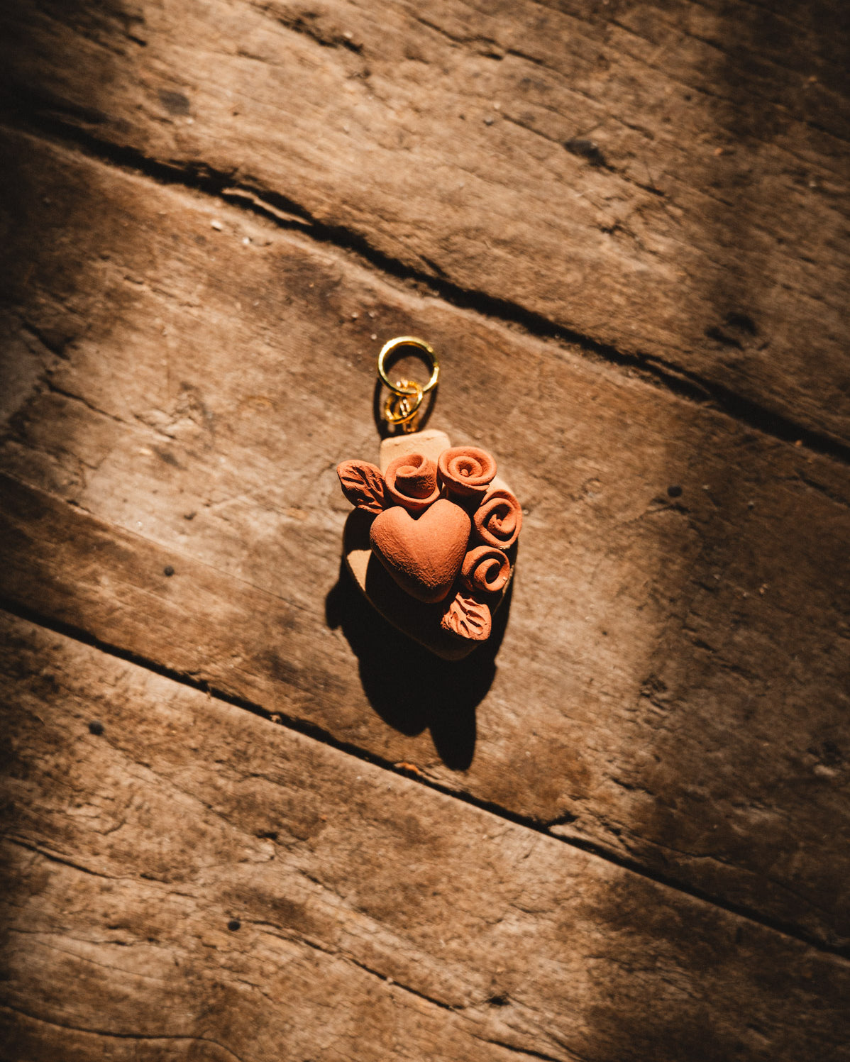 Terra cotta heart-shaped pendant with floral designs on a wooden surface