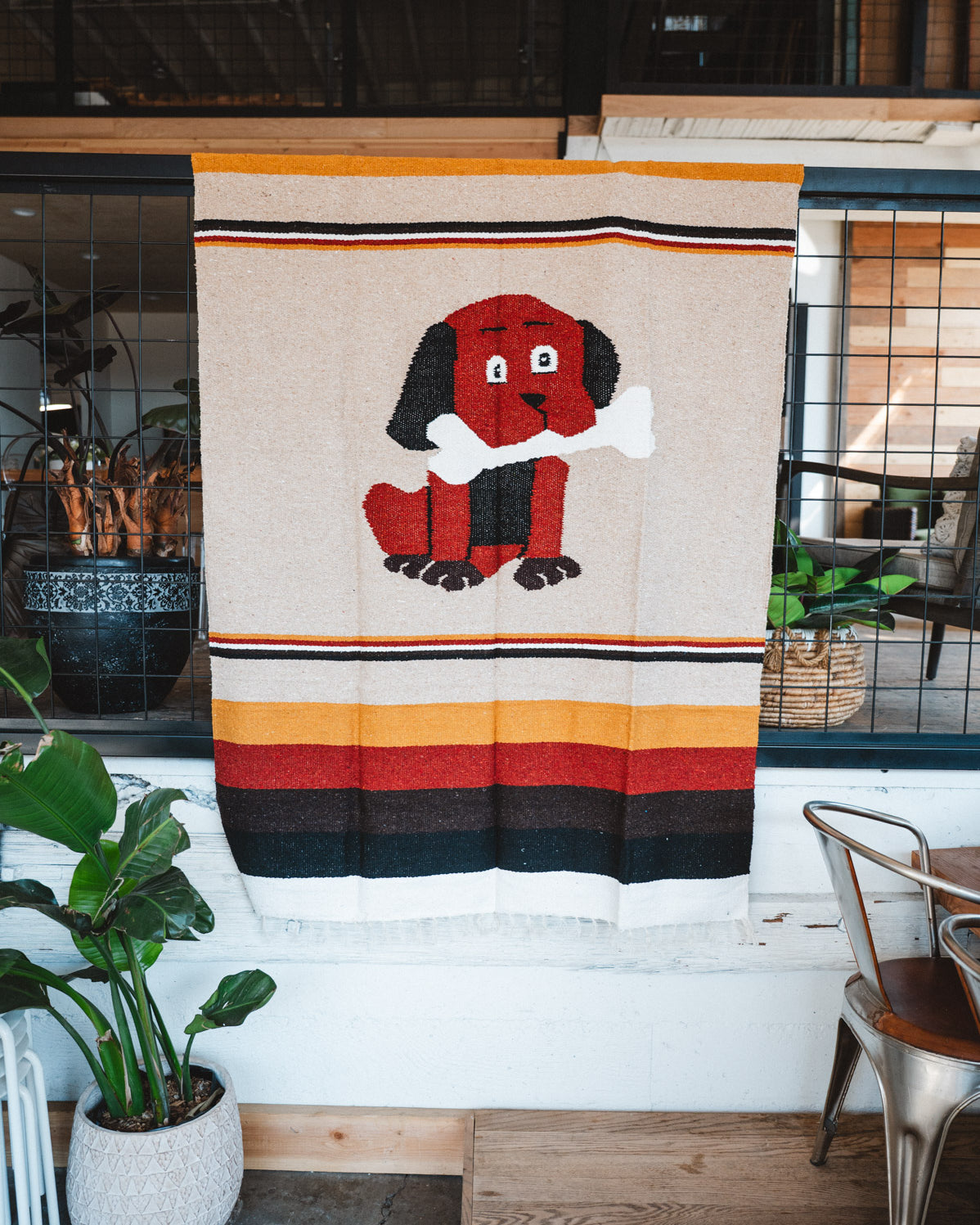 Decorative blanket with a dog design hanging on a wall in a room with plants and furniture.