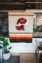 Decorative blanket with a dog design hanging on a wall in a room with plants and furniture.