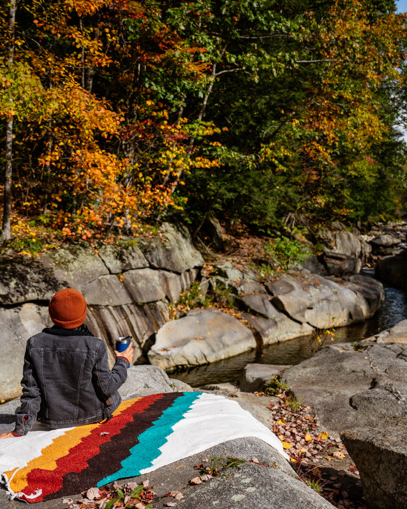 Girl sitting on rocky creekside on top of colorful blanket