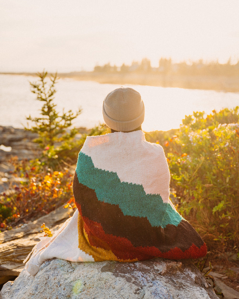 Girl sitting on rock wrapped in blanket at sunset