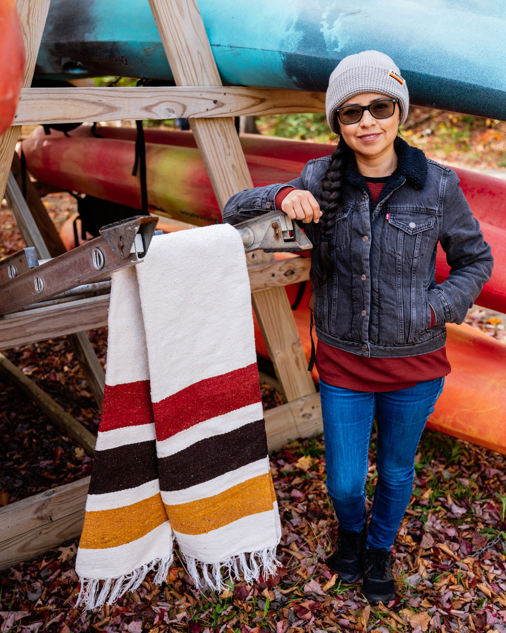 Girl standing in front of a canoe rack next to a striped blanket