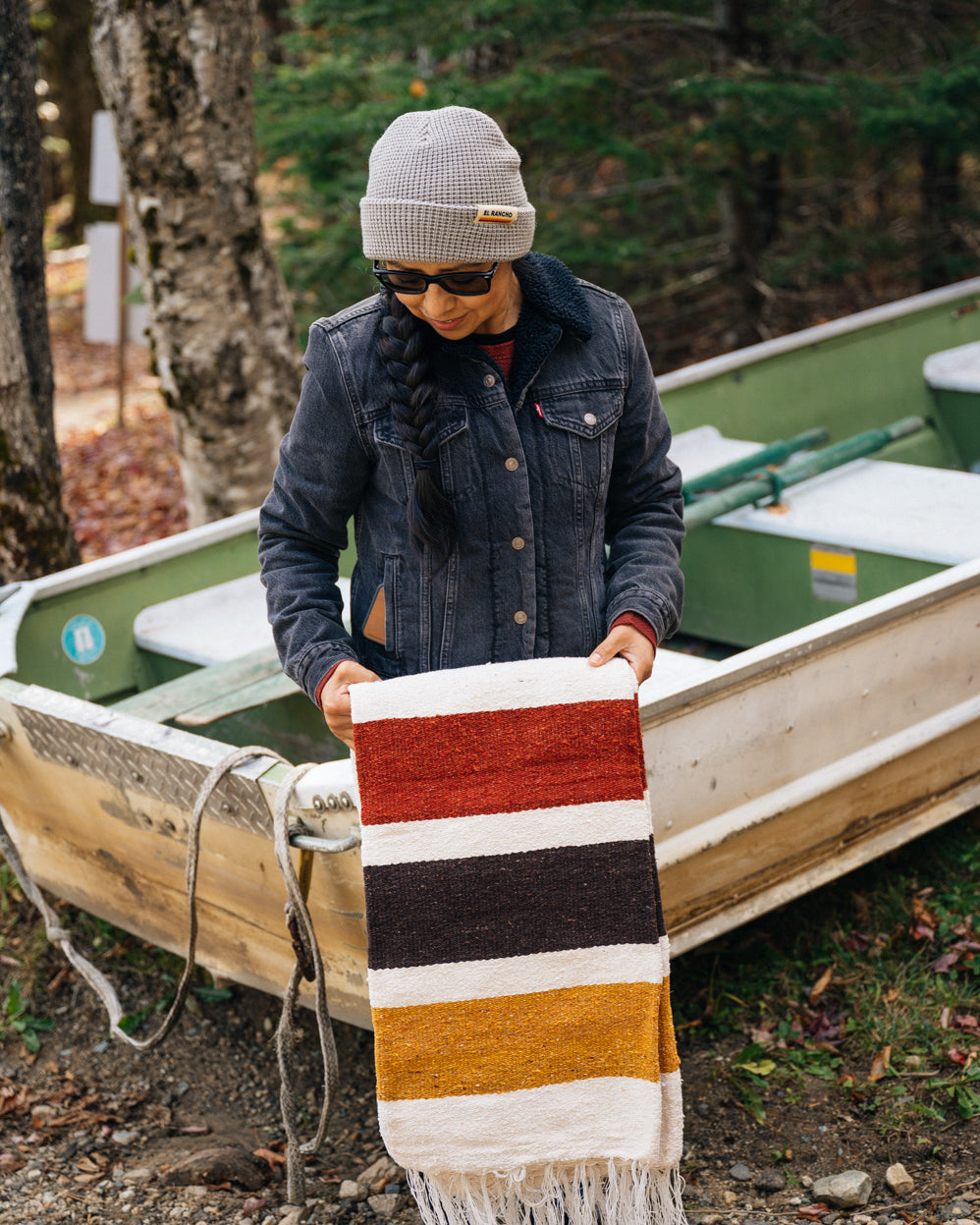 Girl wearing grey beanie and holding striped blanket in front of a boat
