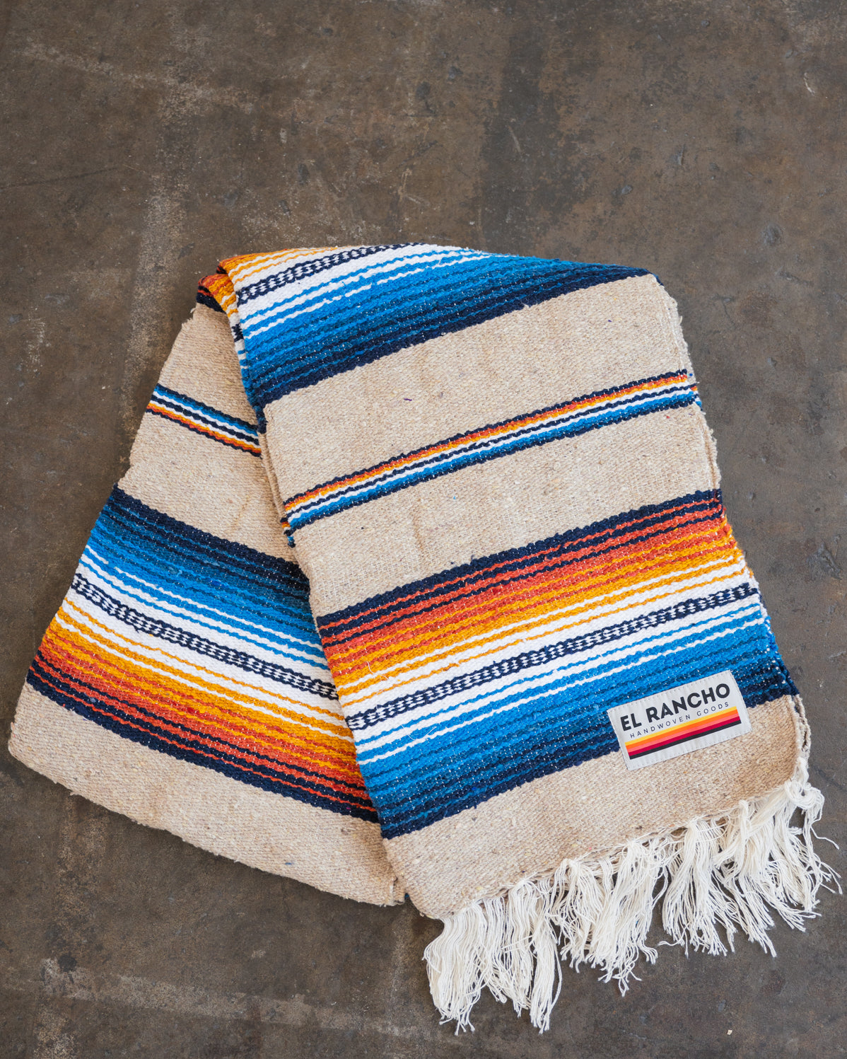 Multicolored Handwoven Saltillo Blanket laying on concrete floor folded in half